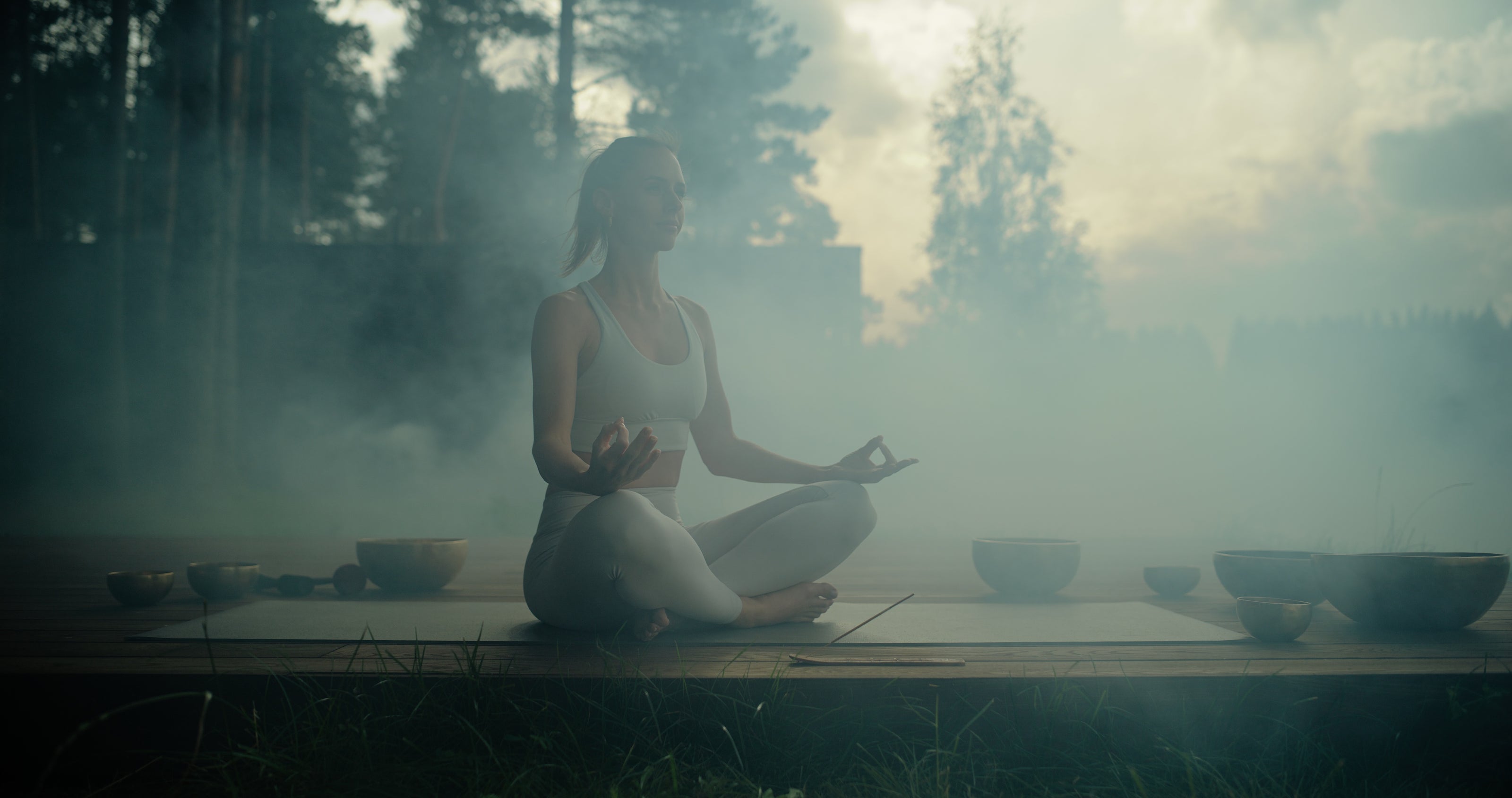A woman meditating in nature with gongs and incense